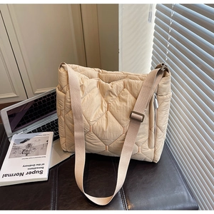 Detail of beige quilted tote bag showing hexagonal stitching and silver side zipper pocket