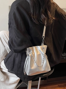 Metallic silver drawstring bucket bag with chain strap shown on a model in urban style