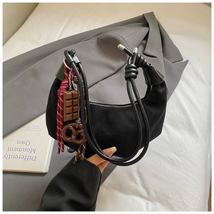 Détail du sac croissant en daim noir avec poignée nouée et breloques chocolat
