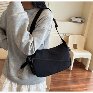 Detail of black nylon crossbody bag with adjustable strap and buckle on model