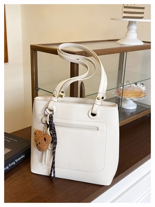 Detail of white lychee leather tote bag with gold hardware and a cute plush bear charm