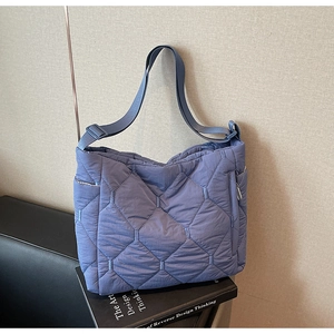 Detail of blue quilted nylon tote bag showing wide strap and diamond stitch texture