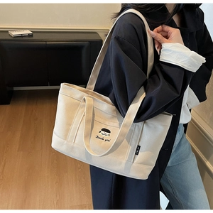 Detail der cremefarbenen Canvas-Tasche mit Cartoon-Stickerei und Markenetikett