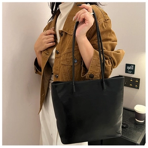 Close-up of minimalist black faux leather tote bag with thin straps on female model