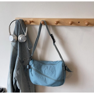 Detail of light blue nylon crossbody bag featuring textured fabric and functional zippers