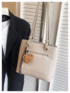 Close-up of beige tote bag with litchi grain texture and a plush bear pendant