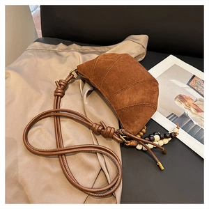 Close-up of suede crescent bag with knotted strap and tricolor beaded tassel charm