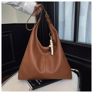 Close-up of brown litchi grain leather tote bag featuring a bohemian wooden bead tassel