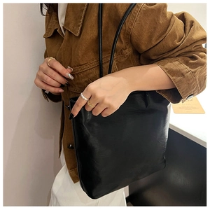 Minimalist black leather tote bag with long shoulder straps shown on a model