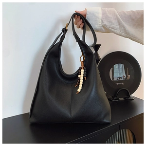 Detail of black lychee grain leather tote bag with ethnic wood bead charm and metal rings