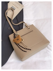Detail of beige lychee grain leather tote bag with plush bear charm and woven strap