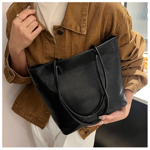 Detail of a large black tote bag with textured leather finish and long handles for shoulder use
