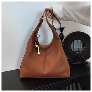 Detail of caramel leather hobo bag with adjustable strap and decorative beaded pendant