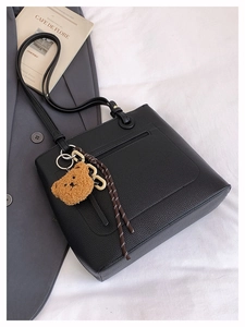 Detail of black pebbled leather tote bag with cute brown bear plush charm and woven strap