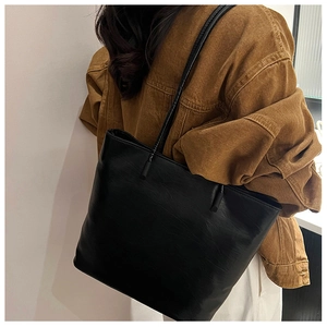 Detail of a black textured faux leather tote bag worn by a model in a casual outfit