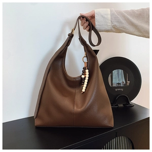 Detailed view of brown leather hobo bag featuring ethnic tassel charm with beads
