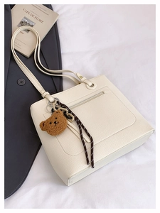 Detail of off-white tote bag in pebbled leather with a cute plush bear charm
