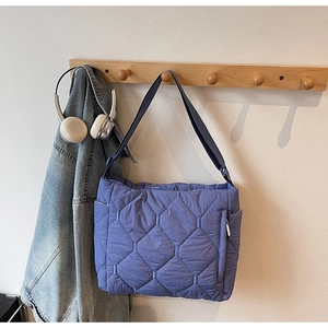 Detail of blue quilted puffer tote bag with side zipper pocket hanging on rack