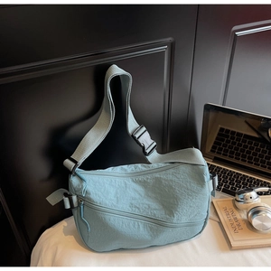 Detail of light blue nylon crescent bag featuring functional zipper pockets and strap