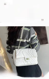 Detailed close-up of white quilted flap bag with golden twist lock and chain strap