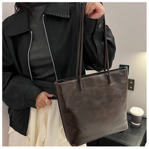 Detail of a dark brown faux leather tote bag with natural grain and long shoulder straps