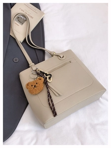 Detail of cream tote bag with back zipper pocket, litchi texture, and bear charm