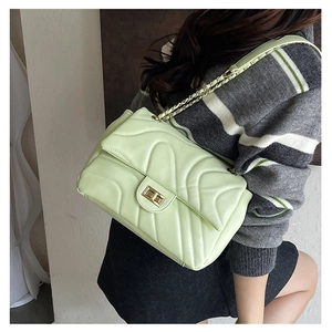 Detail shot of a pistachio green quilted crossbody bag with golden chain and chevron pattern