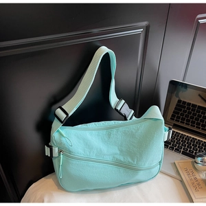 Close-up of mint green nylon crescent bag with multiple zipper pockets and laptop