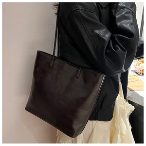Side view of a dark brown leather tote bag worn by a model in a lifestyle setting