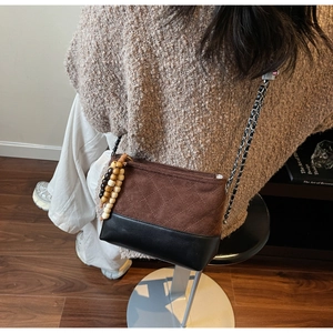 Detail of crossbody bag with brown quilted suede, black leather, and wood bead tassel