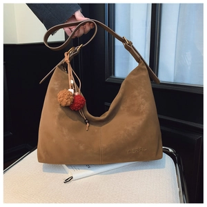 Detail of a brown suede hobo bag with distinctive stitching and fuzzy tassel pendant