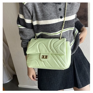 Detail of mint green quilted chain bag worn by model with gold twist lock and V-stitch pattern