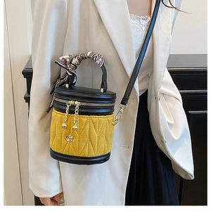 Detail der gelben gesteppten Beuteltasche mit Seidenschal-Griff und Blumenanhänger am Model