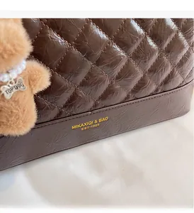 Détail d'un sac fourre-tout en cuir marron matelassé avec breloque ours en peluche