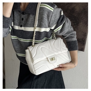 Detail of white wave-quilted shoulder bag featuring a gold twist-lock and chain strap