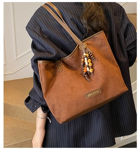 Detail of dark brown tote bag featuring golden metal logo and colorful beaded tassel charm