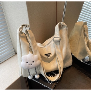 Detail of cream pleated shoulder bag with triangle logo plaque and cloud charm on art book