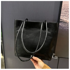 Detail of glossy black tote bag with pleated texture and braided shoulder straps