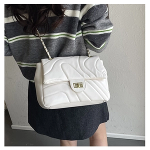Close-up of white chain shoulder bag with wavy stitching and gold twist lock