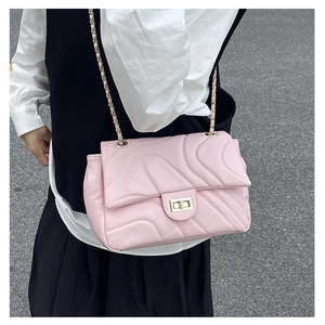 Pink quilted shoulder bag with wave stitching and gold chain strap worn by a model
