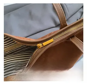 Close-up of golden metal zipper and striped lining on a dark brown suede tote bag