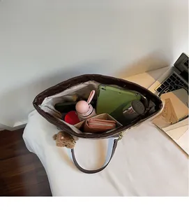 Détail de l'intérieur spacieux d'un cabas marron matelassé avec tablette et objets du quotidien