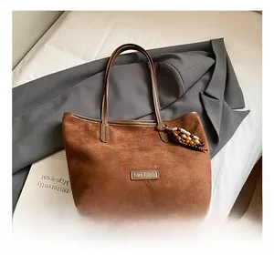 Close-up of brown suede tote bag with leather trim and decorative wooden bead charm