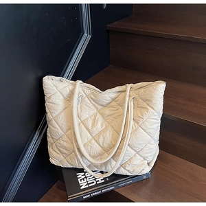 Gros plan sur un grand sac cabas beige matelassé avec surpiqûres en losanges sur bois