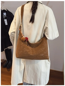 Brown matte suede hobo bag shown on shoulder with plush charm and wide strap detail