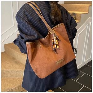 Detail of a brown suede tote bag with ethnic wooden bead tassels and metal logo tag