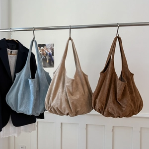 Three suede tote bags in light blue, beige, and tan hanging on a minimalist metal rack