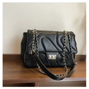 Close-up of black quilted leather surface with golden metal chain and twist lock