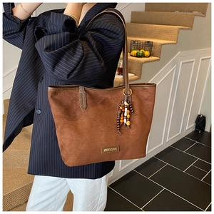 Detail of dark brown suede tote bag with ethnic bead tassel and leather logo patch