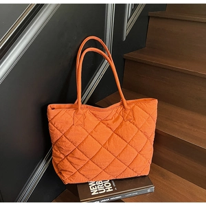 Gros plan d'un sac cabas orange matelassé à losanges sur des marches en bois